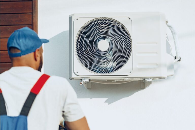 repairman in uniform installing the outside unit of air conditioner