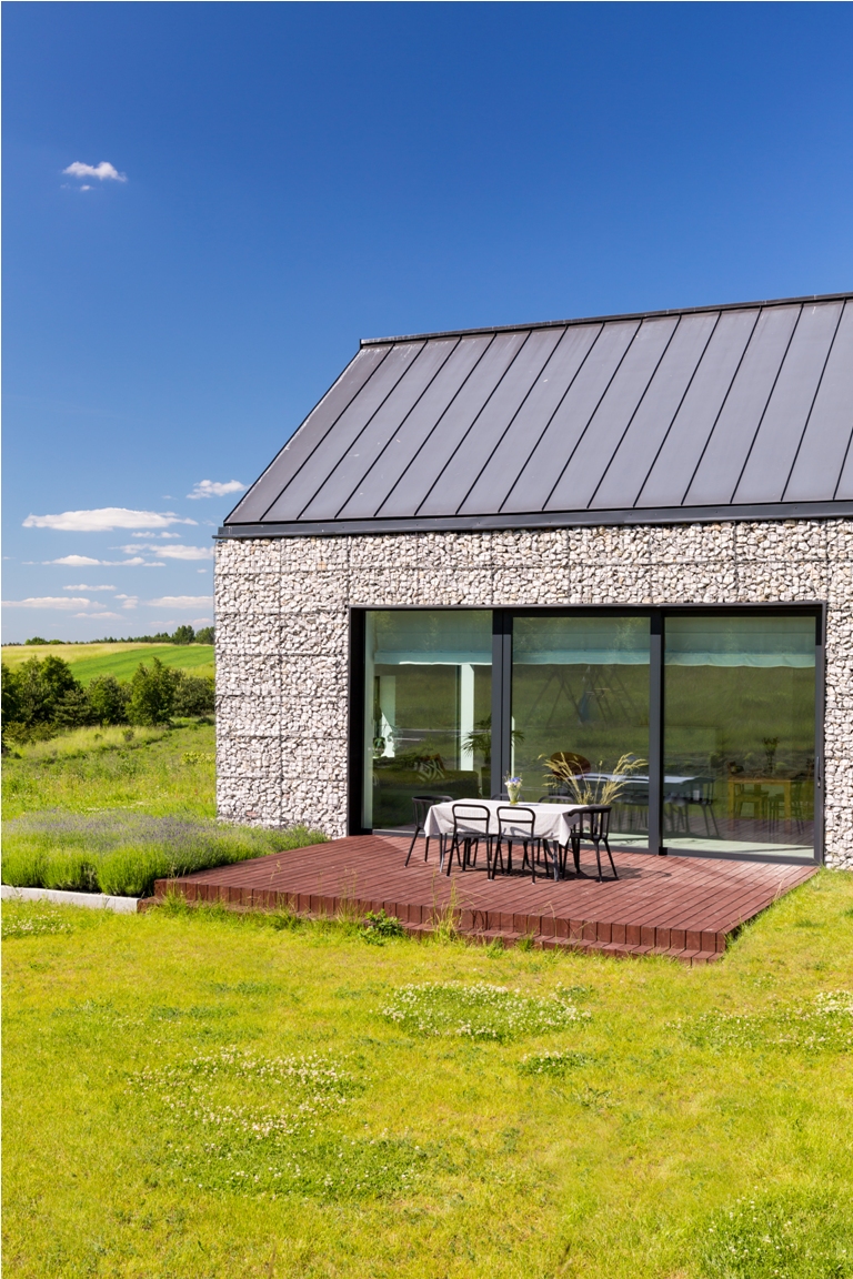 exterior view of a modern stone house with patio and green lawn