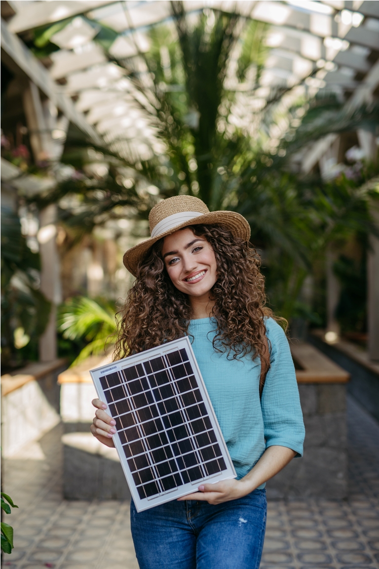 young woman in a botanical garden holding solar panel, concept of green energy.