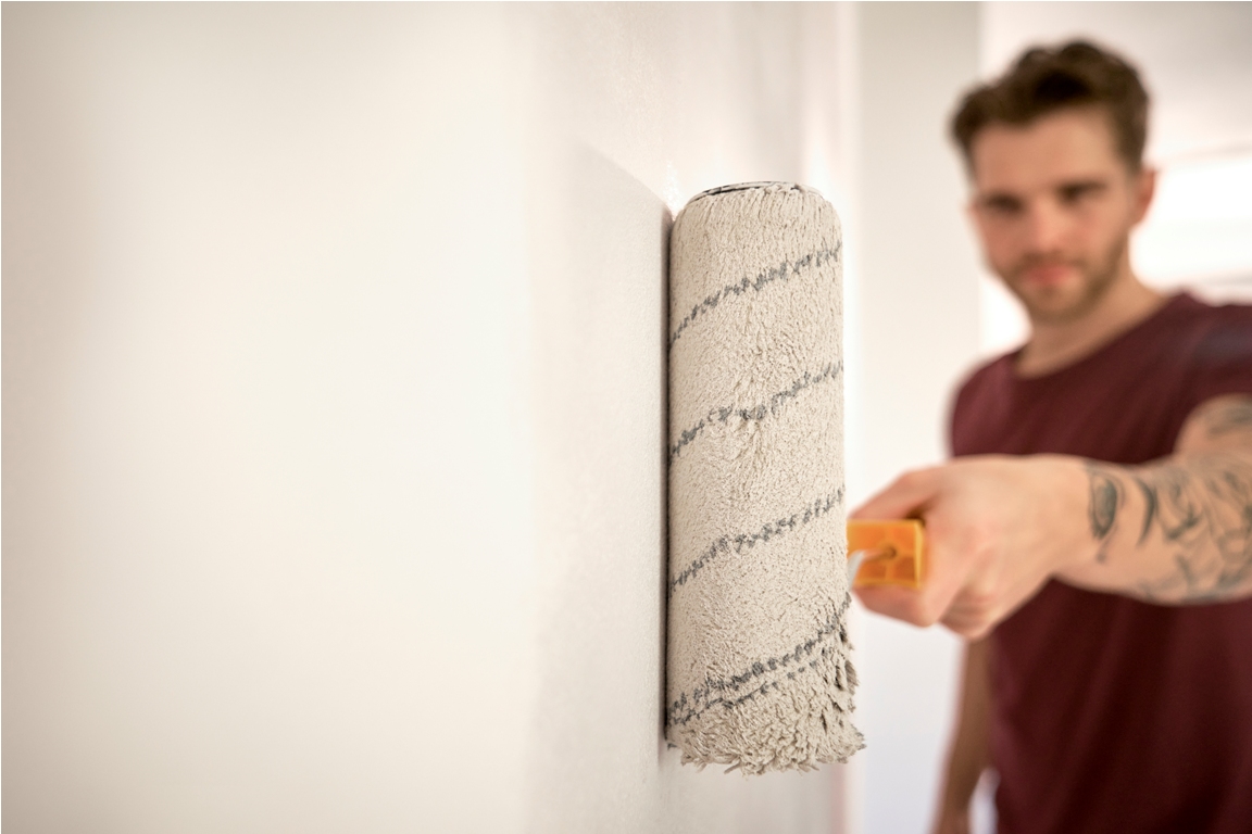 caucasian man painting wall in new house with a paint roller